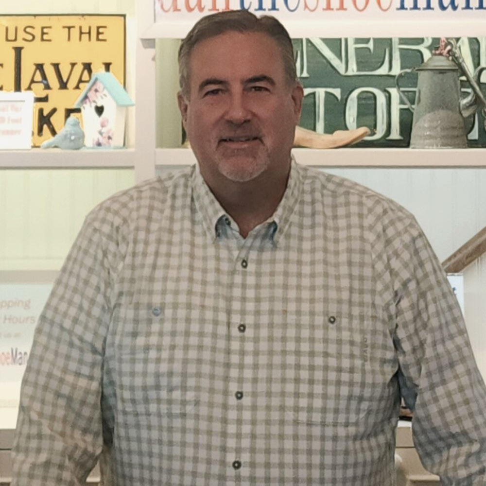 Dan wearing a checkered shirt standing in front of a shelf with decorative items