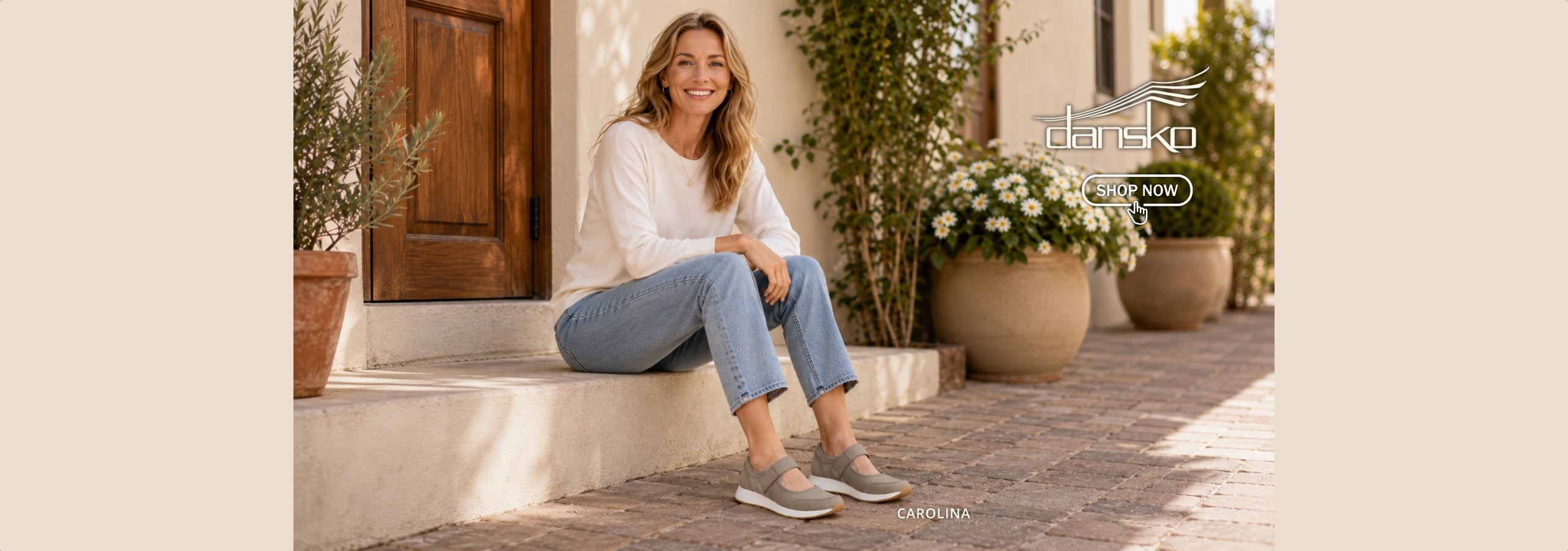 A woman sits on stone steps outdoors wearing a white long-sleeve top, light blue jeans, and gray slip-on shoes. The scene includes potted plants and a wooden door, with the brand name 'DaNSKO' visible in the upper right.
