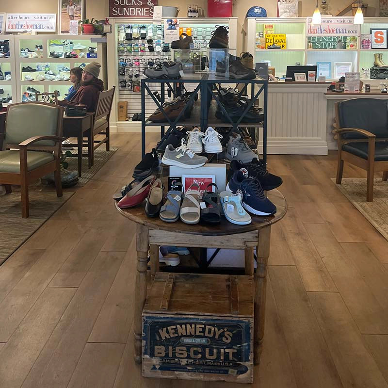 Shoes displayed on a table in a store with chairs and shelves in the background